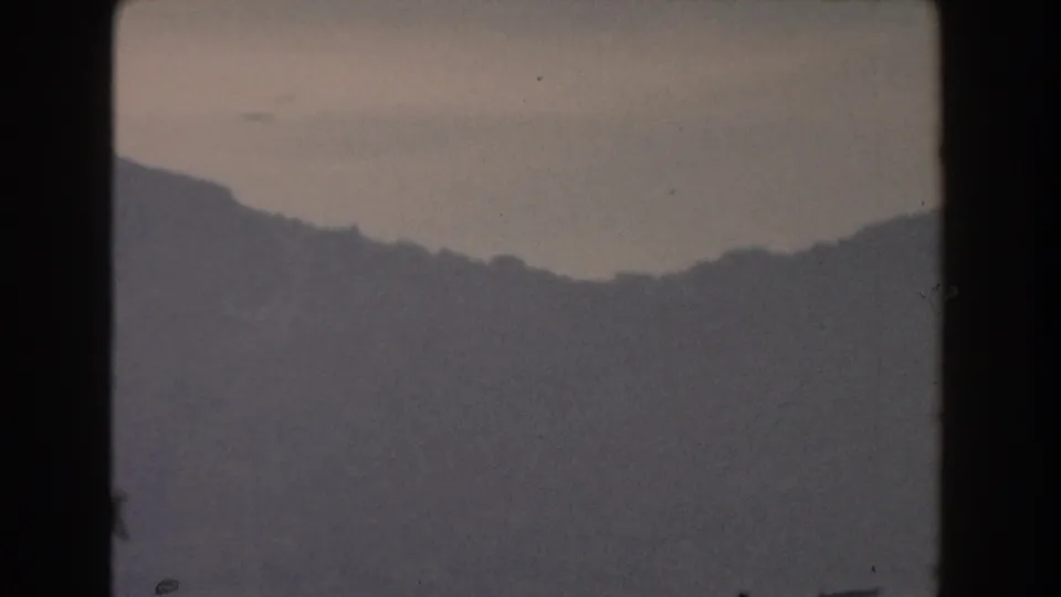 A 1959 Gibraltar 8mm view of a low dark ridge in fog, with muted color, soft contrast, and visible film wear.