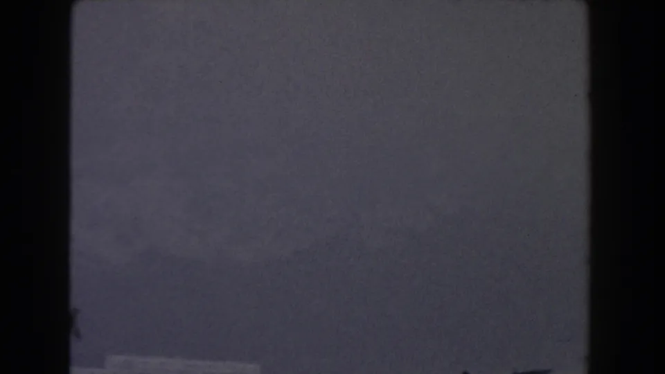 1959 Gibraltar frame showing a dark mountain face softened by fog, with subdued blue-grey tones and visible 8mm frame edges.