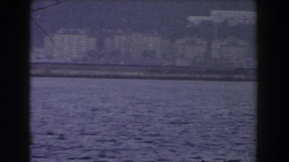 A soft 8mm travel view of Gibraltar's coast, with dark blue sea in front and hazy waterfront structures beyond.