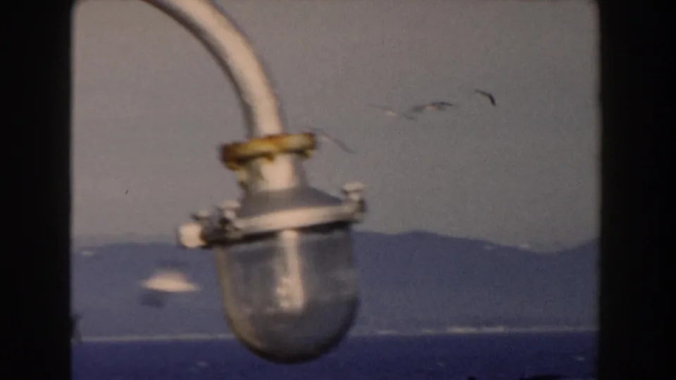 1959 Gibraltar boat view with a weathered lamp fixture in front of distant hills and sea.