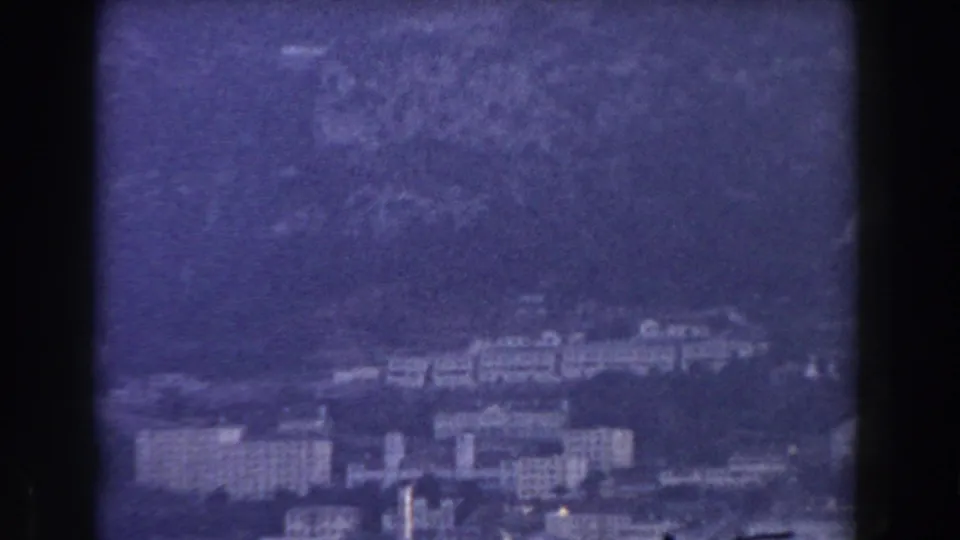 High-vantage 1959 Gibraltar home-movie frame showing buildings at the base of the Rock under haze.