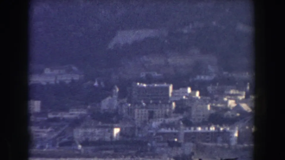 1959 Gibraltar home-movie frame showing a distant townscape at the foot of the Rock, with hazy sky and soft blue film color.
