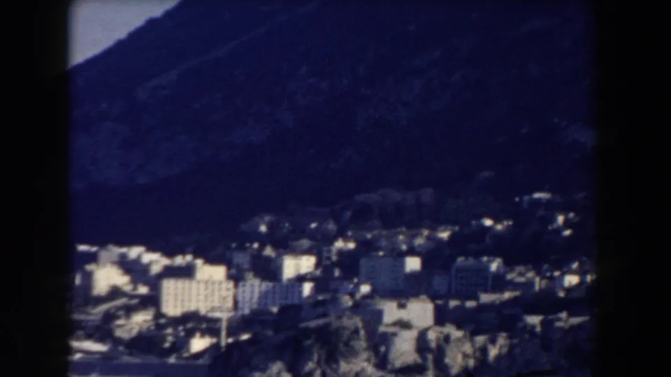 1959 Gibraltar frame showing clustered white buildings and stone-toned structures against a steep, shadowed mountain base.