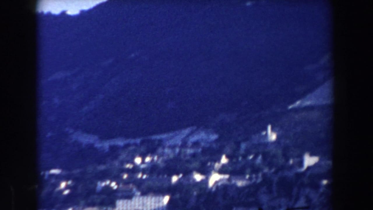Hillside settlement and bright buildings seen across a dark valley slope.