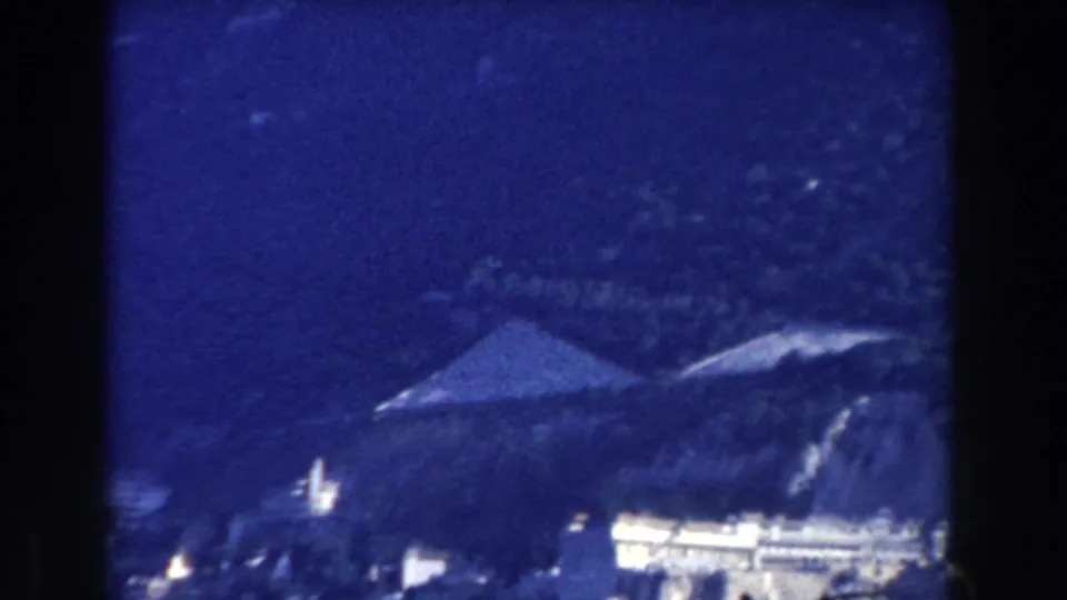 Blue-shifted 1959 8mm frame likely in Gibraltar, with a conical roof form among hillside structures and trees.