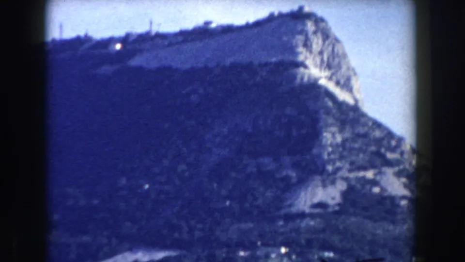 Likely Gibraltar 1959 home-movie frame showing a rocky mountain face, dark slopes, and small buildings below.