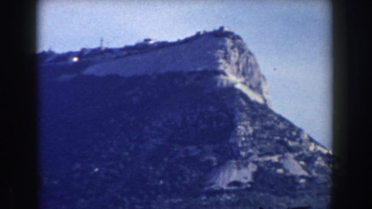 Rocky Gibraltar hillside above waterfront buildings, seen through dark film frame edges.