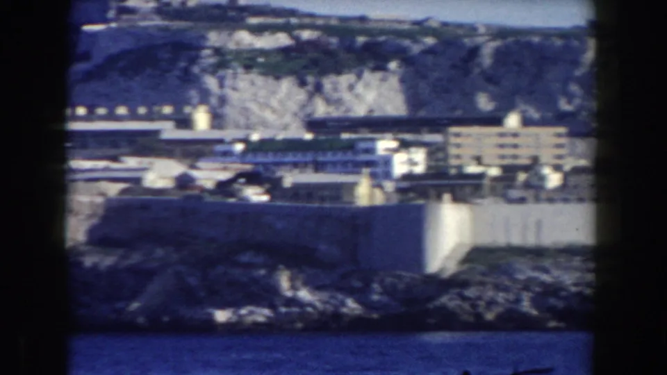 1959 Gibraltar frame showing coastal water, pale walls, waterfront buildings, and the rocky base of the Rock.