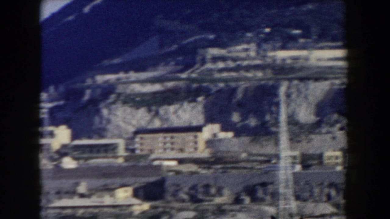 Distant buildings below a steep rocky mountain with dark film borders.