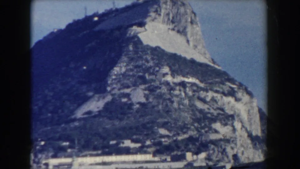1959 Gibraltar frame showing the Rock rising above low buildings, with grain, soft focus, and blue-tinted home-movie color.