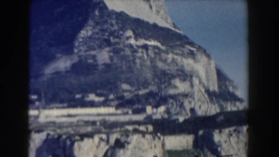 Gibraltar home-movie frame with cliff textures, lower buildings, and the Rock filling most of the view in faded 8mm color.