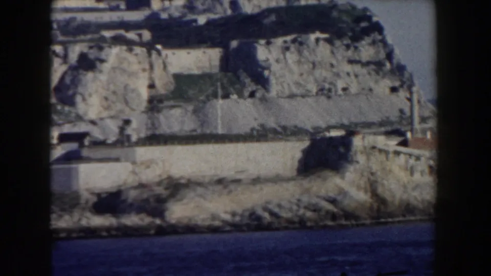 1959 Gibraltar frame with terraced coastal defenses, rough rock formations, and water at the base of the Rock.