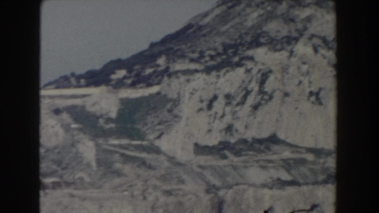 1959 Gibraltar 8mm frame showing pale rock faces, dark seams, and a steep mountain slope under a washed sky.