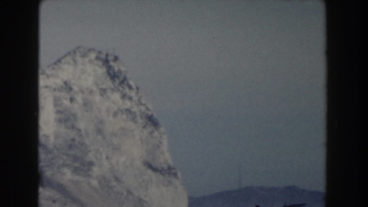 Snow-covered rocky mountain peak beneath a pale sky, seen through an 8mm film frame.