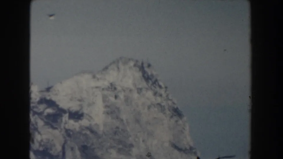 1959 8mm frame of a rugged snow-covered mountain peak, softly exposed against a muted sky.
