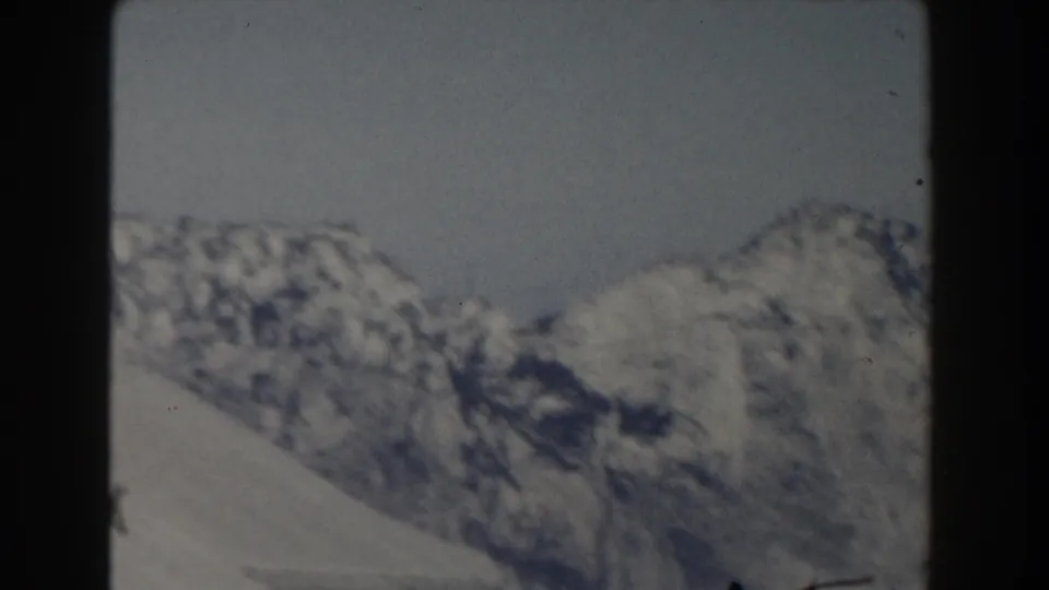 1959 8mm frame showing a snow-covered ridge line and darker mountain slope in a handheld landscape view.