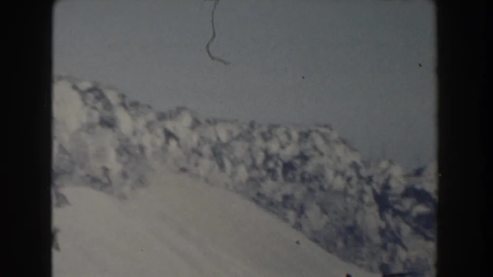 1959 8mm frame of a distant snow-covered ridge with exposed rock and visible film dust near the sky.