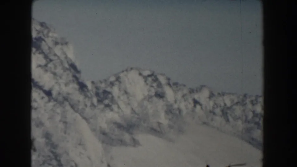 1959 Gibraltar-labeled 8mm frame showing distant snowy mountain peaks, pale sky, and shadowed rock faces.