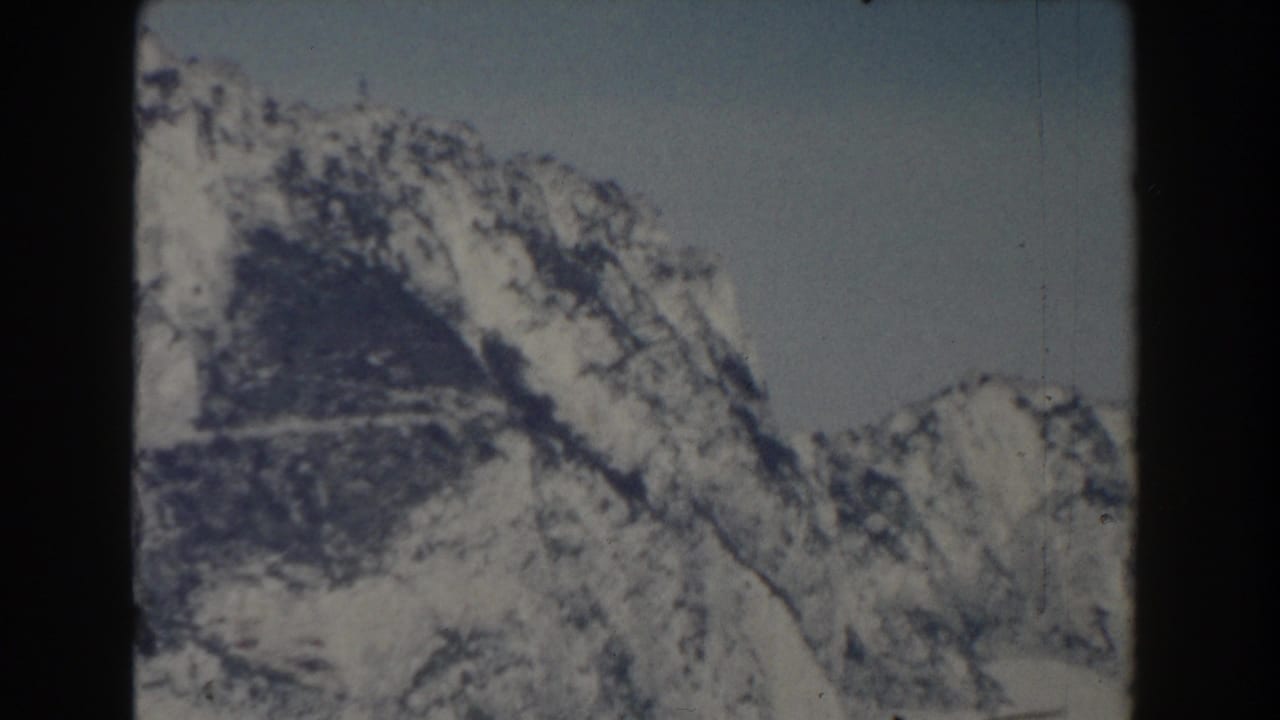 Tall snow-streaked mountain face with pale sky and dark rock texture.