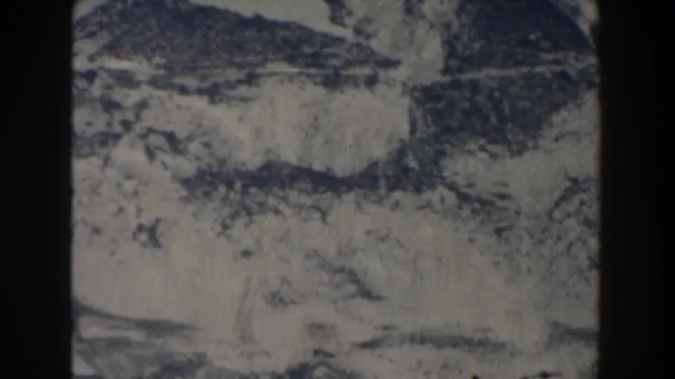 1959 Gibraltar-labeled 8mm frame of snowy mountain terrain with dark ridges, pale sky, and soft film texture.