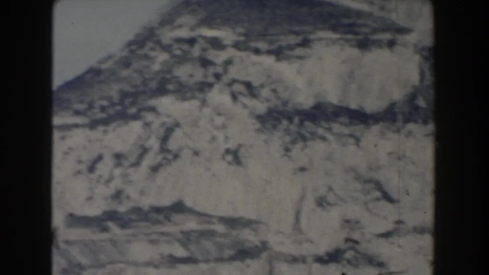 1959 8mm view of Gibraltar's pale rocky cliff face and lower slopes, framed by dark film borders.