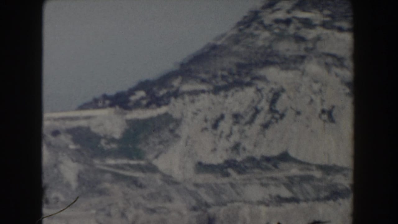 Steep rocky hillside with pale exposed stone and lower terrain visible.