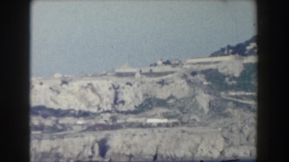 Bright 1959 8mm frame of Gibraltar's pale limestone cliffs and hillside, with lower terrain visible near the bottom edge.