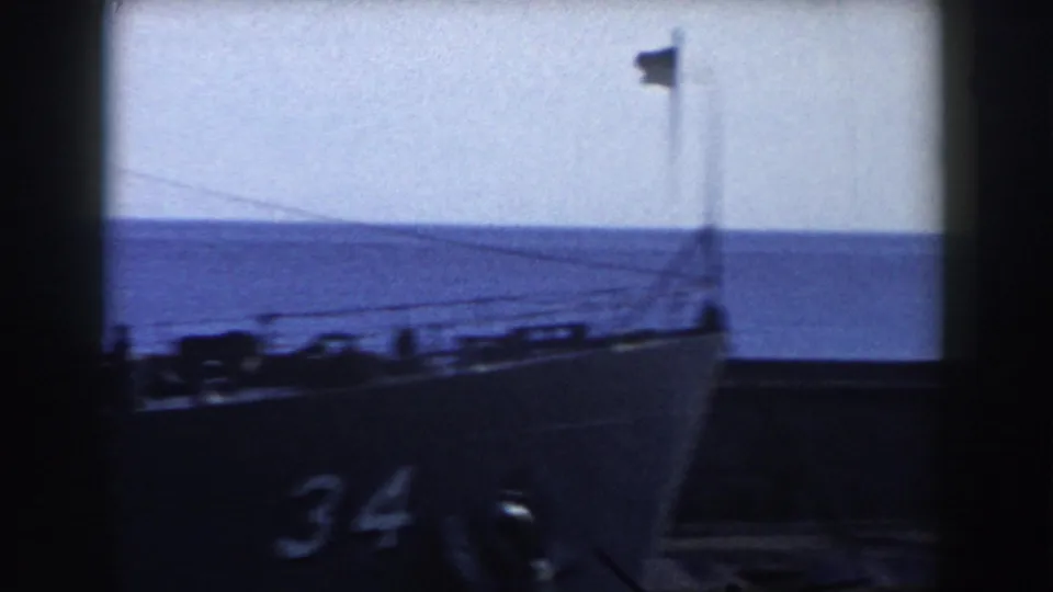 1959 Gibraltar waterfront frame showing a naval vessel bow marked 34, with railing, flag, sea, and sky visible.