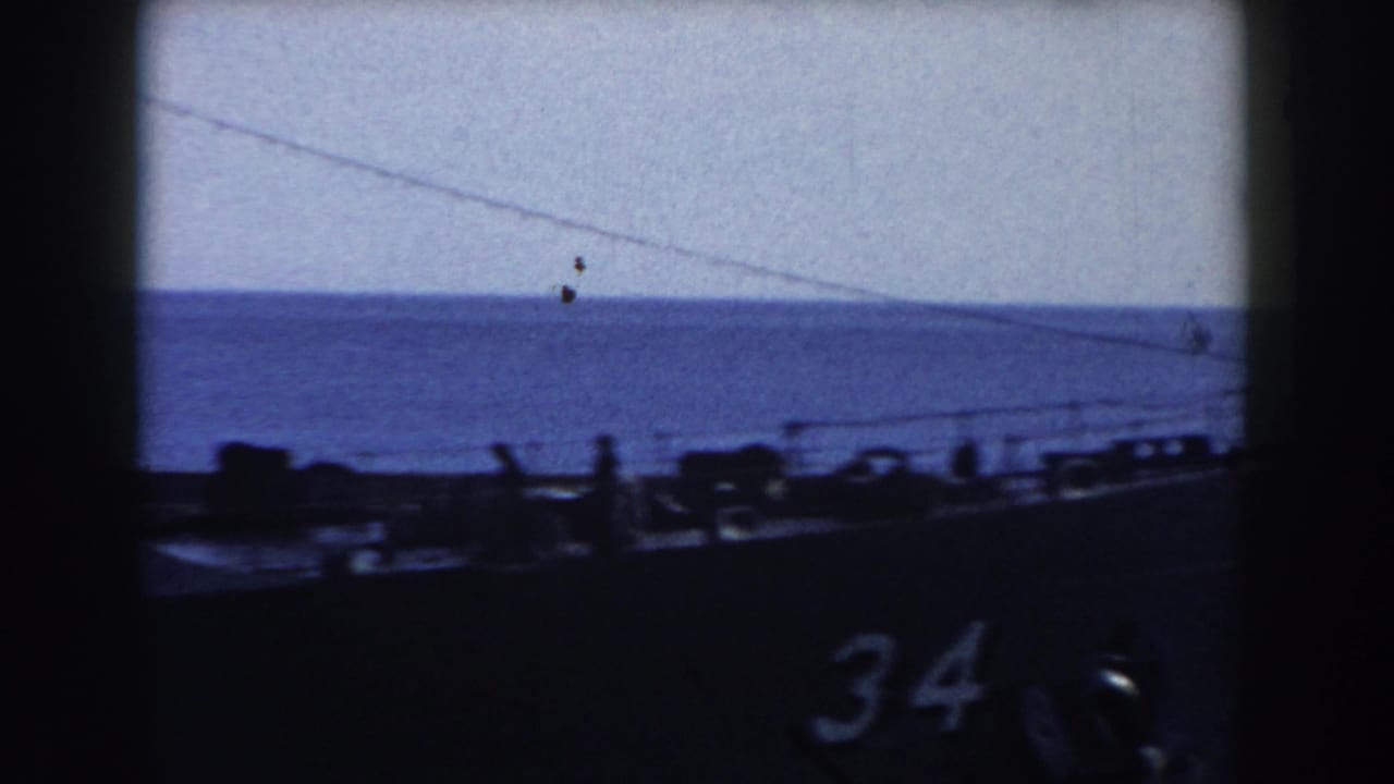 Warship hull with number 34, deck silhouettes, and calm sea beyond.