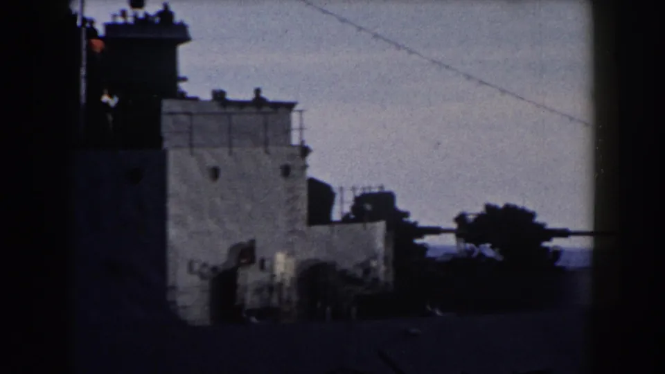 1959 Gibraltar footage frames the warship superstructure with silhouetted crew on the upper deck and a gun turret visible near the lower right.