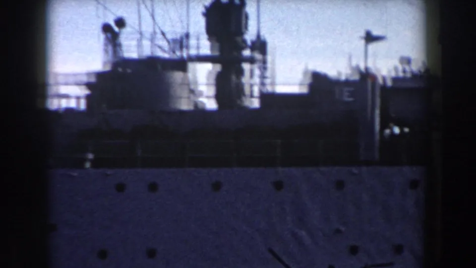 The final 8mm frame shows the warship's upper deck with railings, mast-like fittings, silhouetted crew, and hull portholes below.