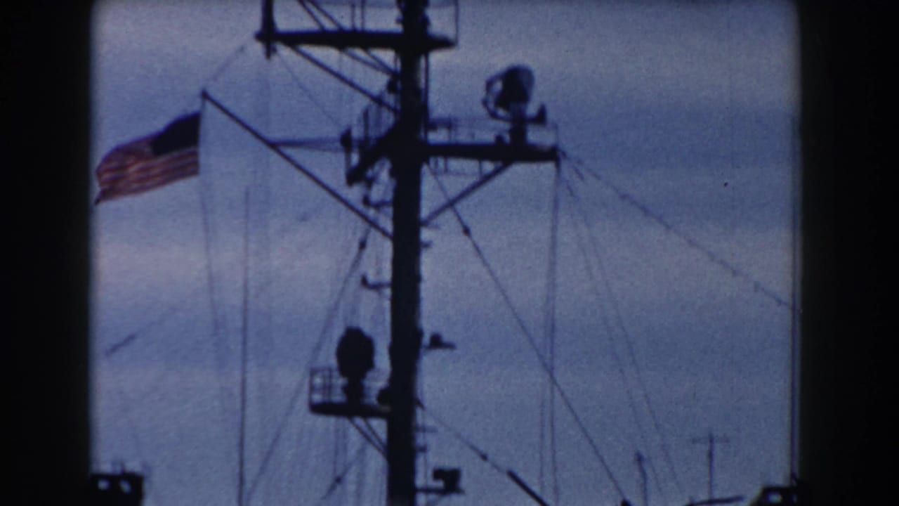 1959 Gibraltar 8mm frame with a U.S. flag near a ship mast, rigging, and antenna equipment in silhouette.