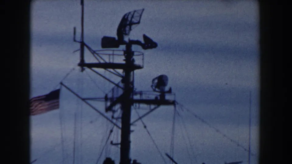 1959 Gibraltar 8mm view of a ship mast with radar array, antennas, rigging, and a U.S. flag at the edge of frame.