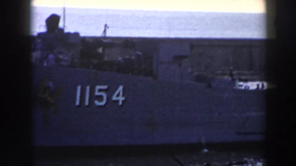1959 Gibraltar 8mm frame showing the side of a U.S. Navy vessel with hull number 1154 and harbor water below.