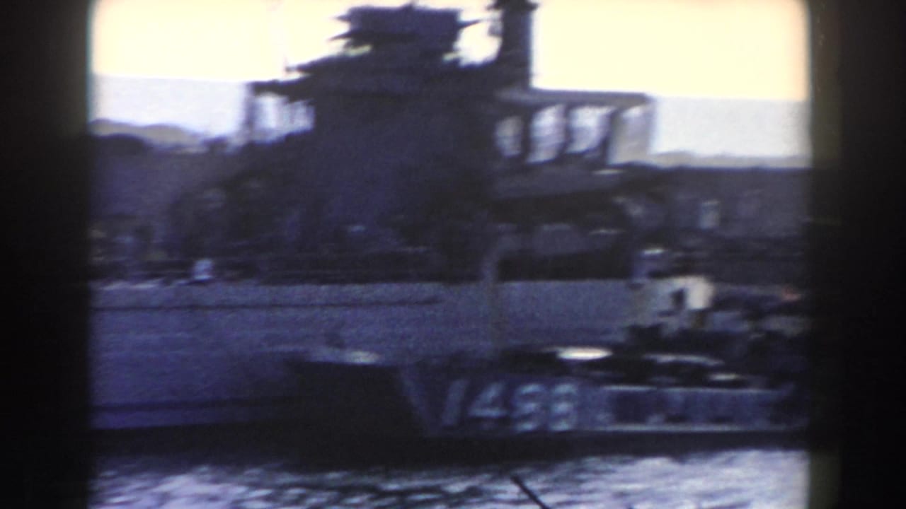 A docked naval vessel in Gibraltar appears in soft blue 8mm footage, with superstructure, harbor water, and distant hills behind it.