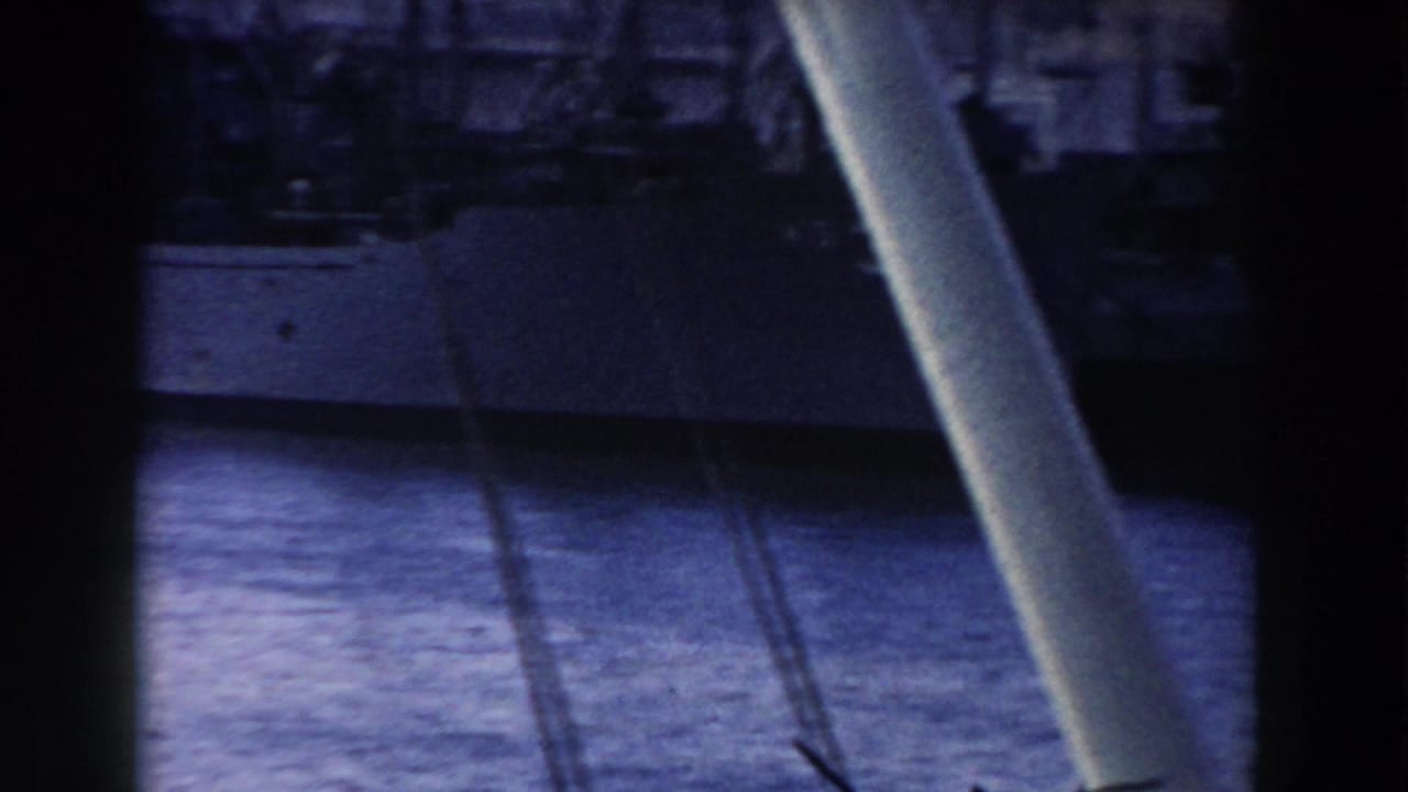 Obstructed 1959 Gibraltar harbor frame with a vessel hull across the water and port structures beyond.