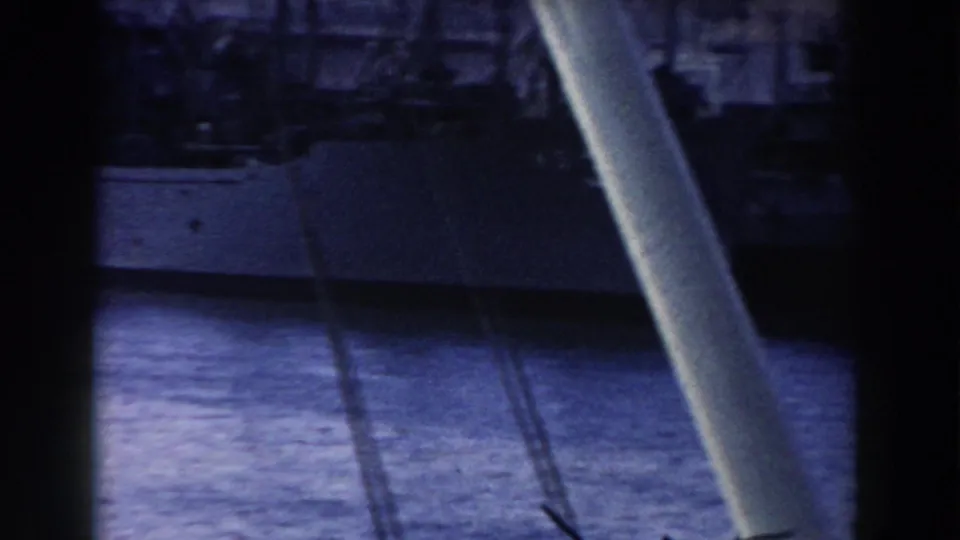 Obstructed 1959 Gibraltar harbor frame with a vessel hull across the water and port structures beyond.