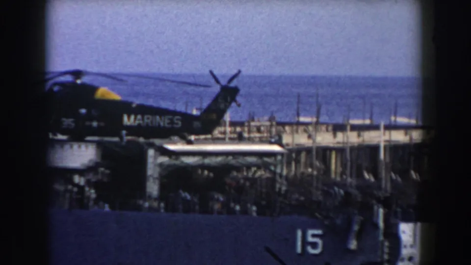 1959 Gibraltar frame showing a U.S. Marines helicopter on a ship deck, with hull number 15 and harbor water behind it.