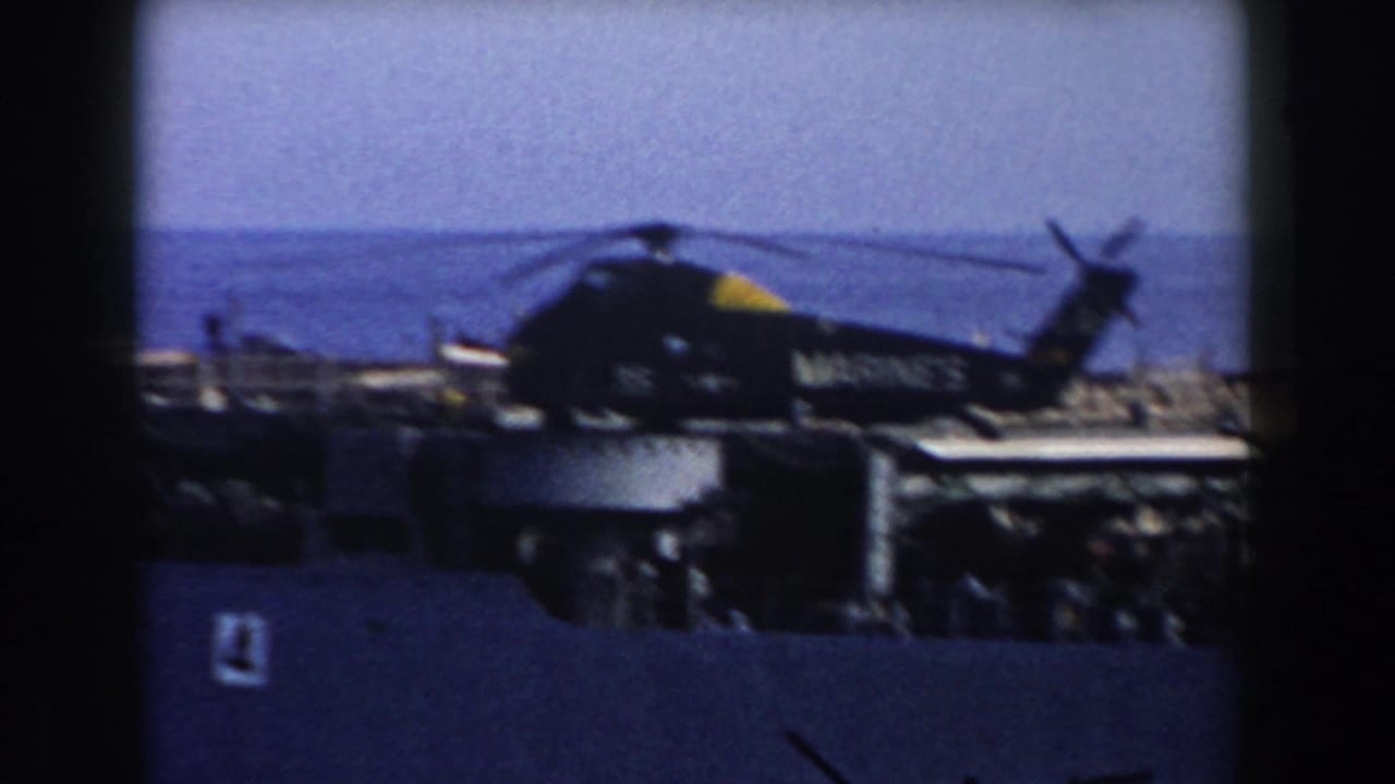A soft 1959 8mm frame shows the Marine Corps helicopter on a naval vessel deck with open water beyond.