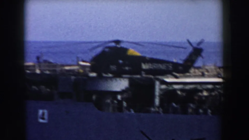 A soft 1959 8mm frame shows the Marine Corps helicopter on a naval vessel deck with open water beyond.