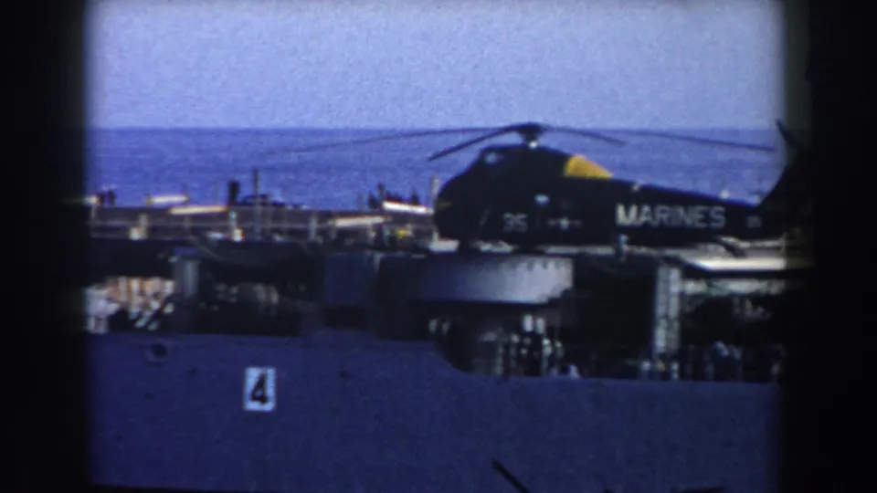 1959 8mm frame of the Marine Corps helicopter parked on a ship deck, with hull number 4 visible below and sea beyond.