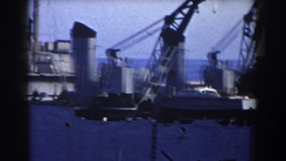 1959 Gibraltar harbor view with a grey ship, cranes, deck structures, and water in soft 8mm color.