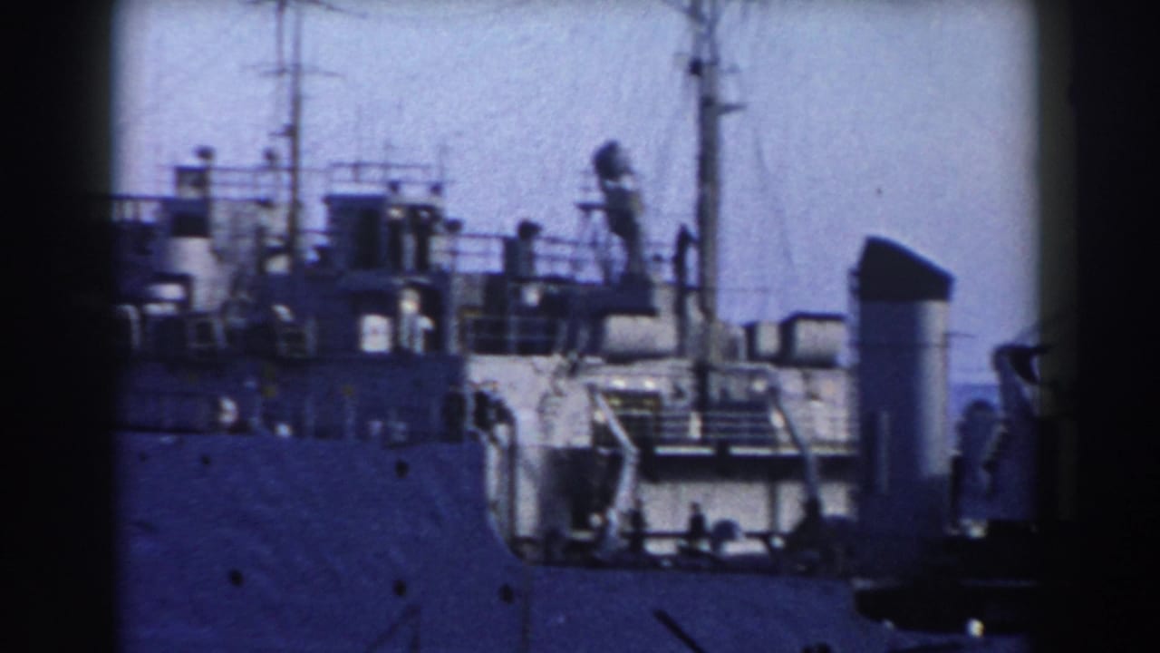 Close view of a grey ship deck with mast, railings, and crane equipment.