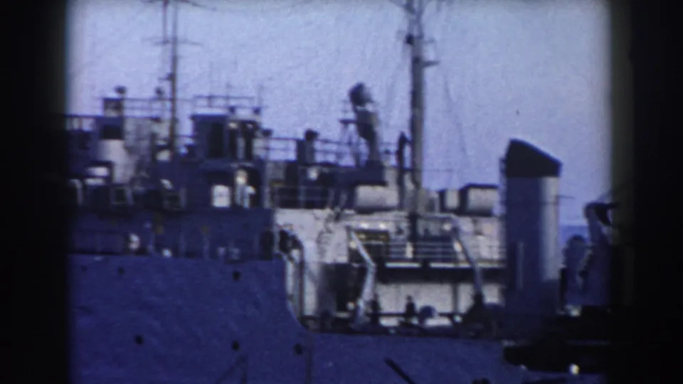 Grey ship deck in Gibraltar harbor with mast lines, railings, cranes, and small distant figures or equipment shapes.