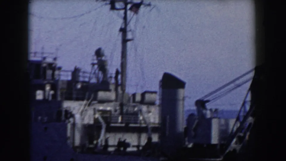 1959 Gibraltar harbor footage showing the ship's deck structures, a funnel, mast lines, and crane boom in grainy 8mm color.