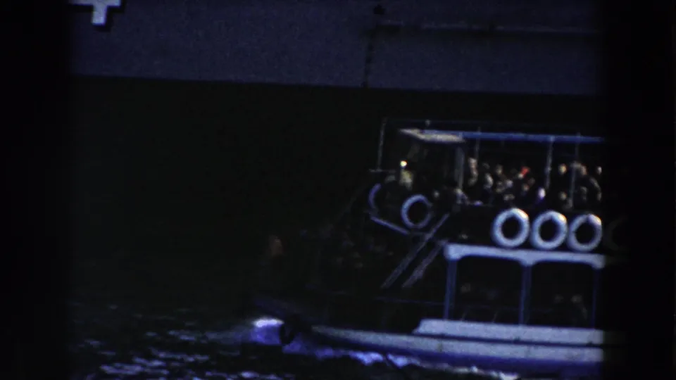 Brown-and-white harbor tugboat passes near a larger grey ship in Gibraltar, with passengers or crew faintly visible aboard.