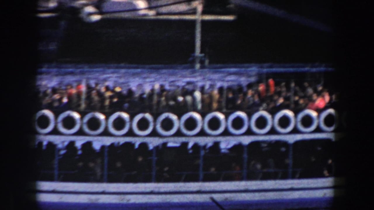 Crowded ferry deck with white life rings moving across dark water.