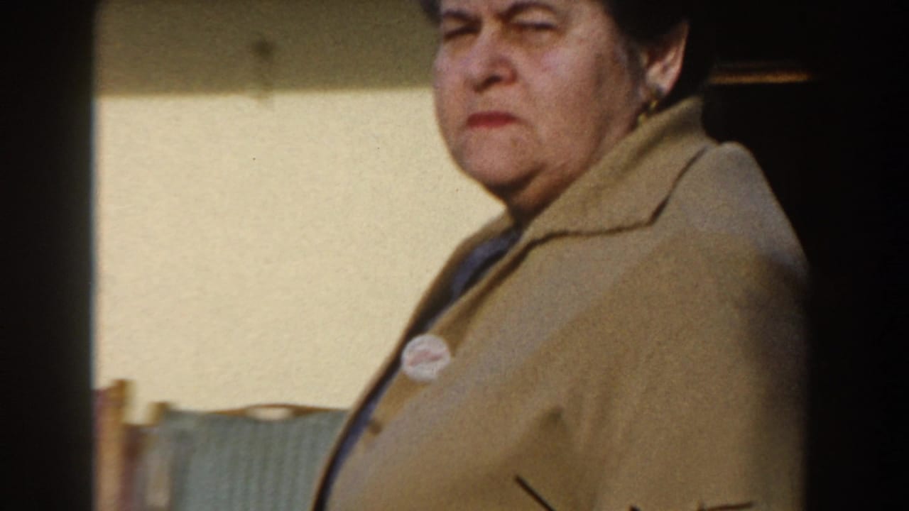 Older woman in a beige cardigan near a ship doorway, seen in close handheld framing.