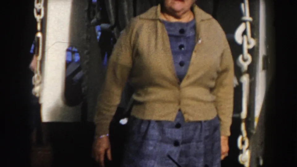 Cropped view of the woman standing on the ship deck, with a white chain and shadowed machinery visible nearby.