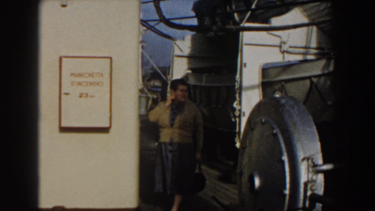 Woman in a yellow sweater stands on a ship deck beside a white fire-hose cabinet sign.